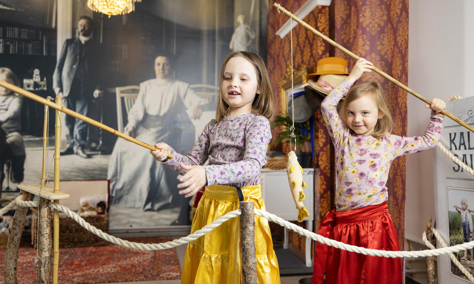 Kaksi tyttöä leikkii ongilla vanhan ajan interiöörissä.