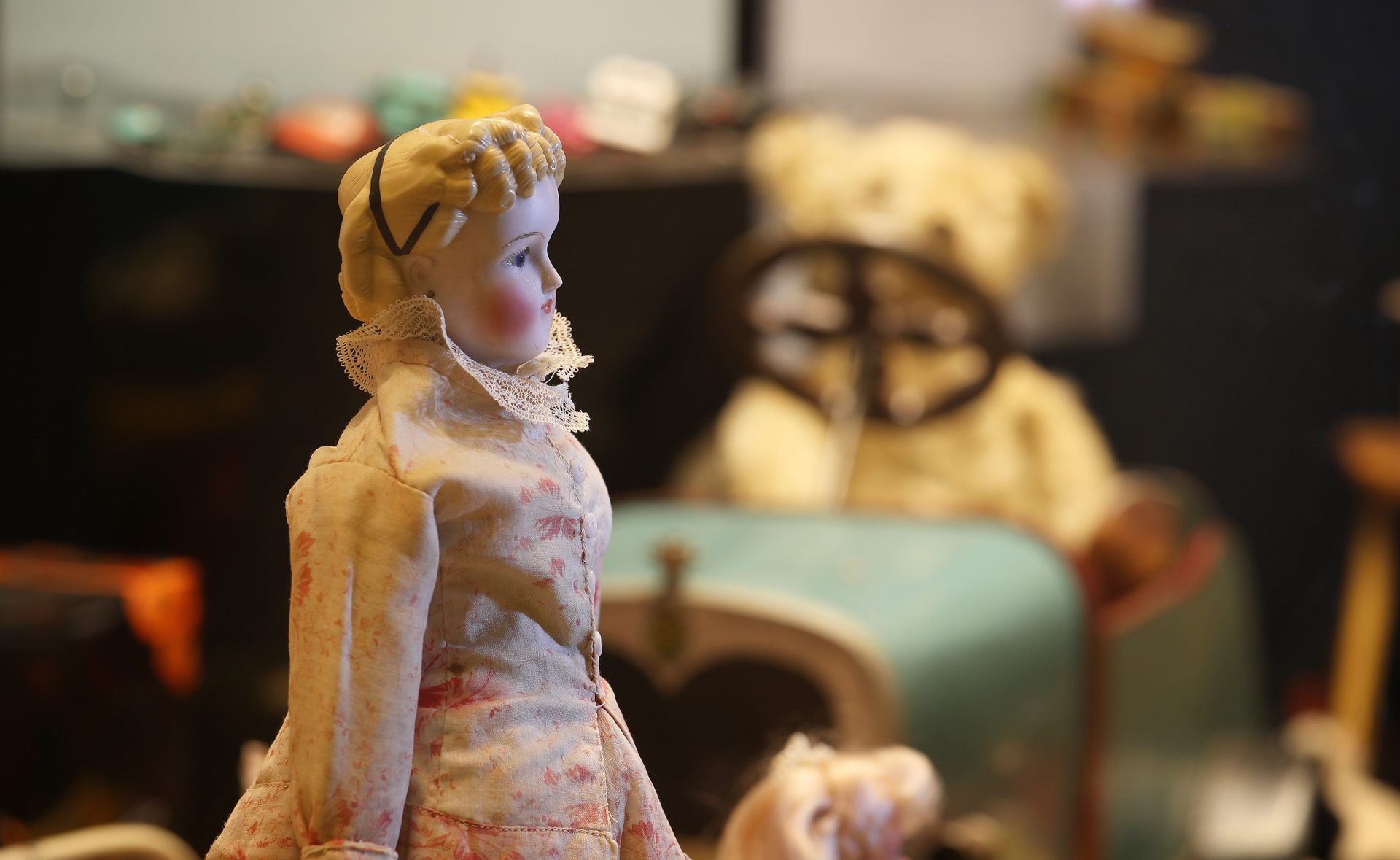 Etualalla vanha nukke, taustalla polkuauto, jonka kyydissä nalle.