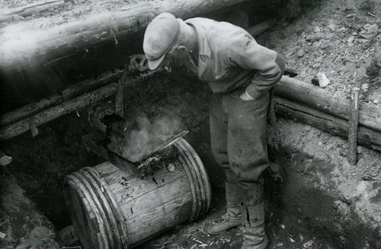 Mies laskee tervaa haudasta tynnyriin.