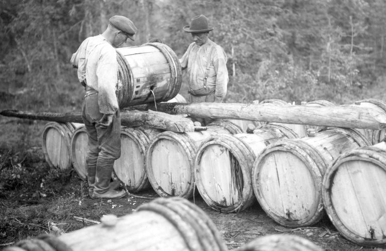 Kaksi miestä täyttämässä vajaita tervatynnyreitä.