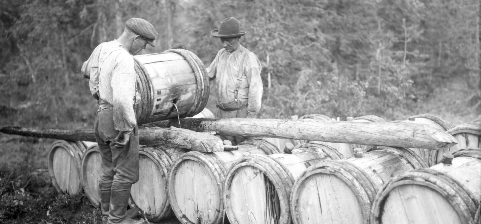 Kaksi miestä täyttää tervatynnyreitä.