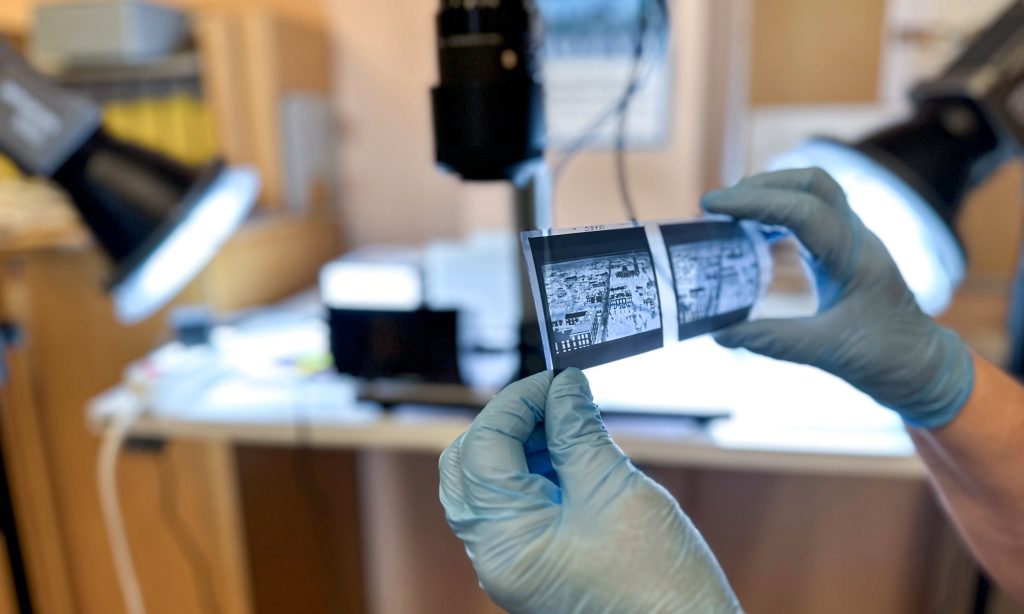 Arkistonhoitaja tarkastelee hanskat kädessä vanhaa isokokoista valokuvanegatiivia.