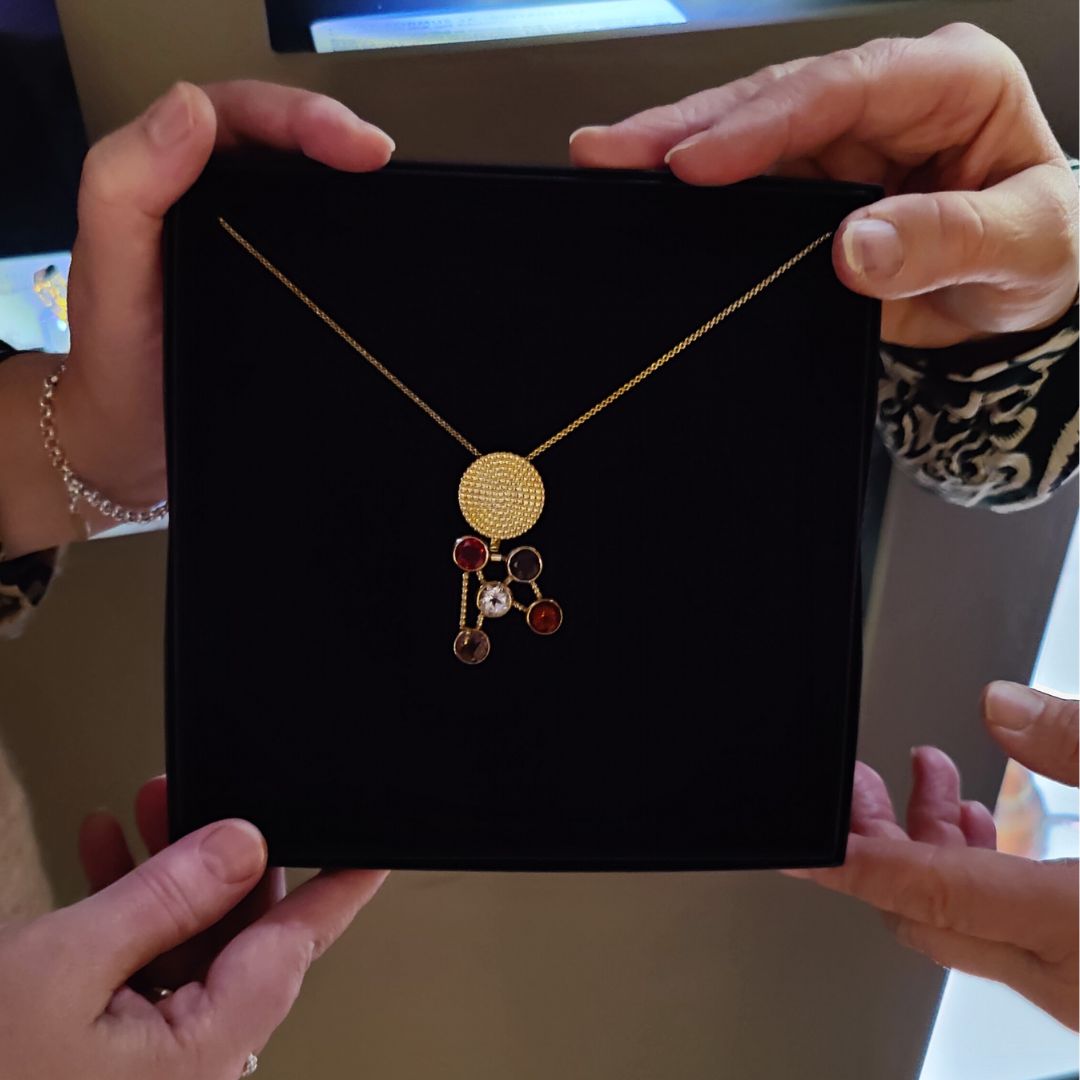 Pyöreä kultainen koru, josta riippuu paljon pyöreitä jalokiviä.