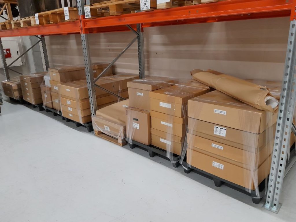 Varastohyllyjen alaosassa pahvilaatikoita pakattuna.