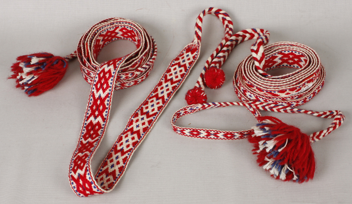 Punavalkoiset poimintakuvioiset pirtanauhat kerällä. Pirtanauhojen päässä punavalkoiset tupsut.