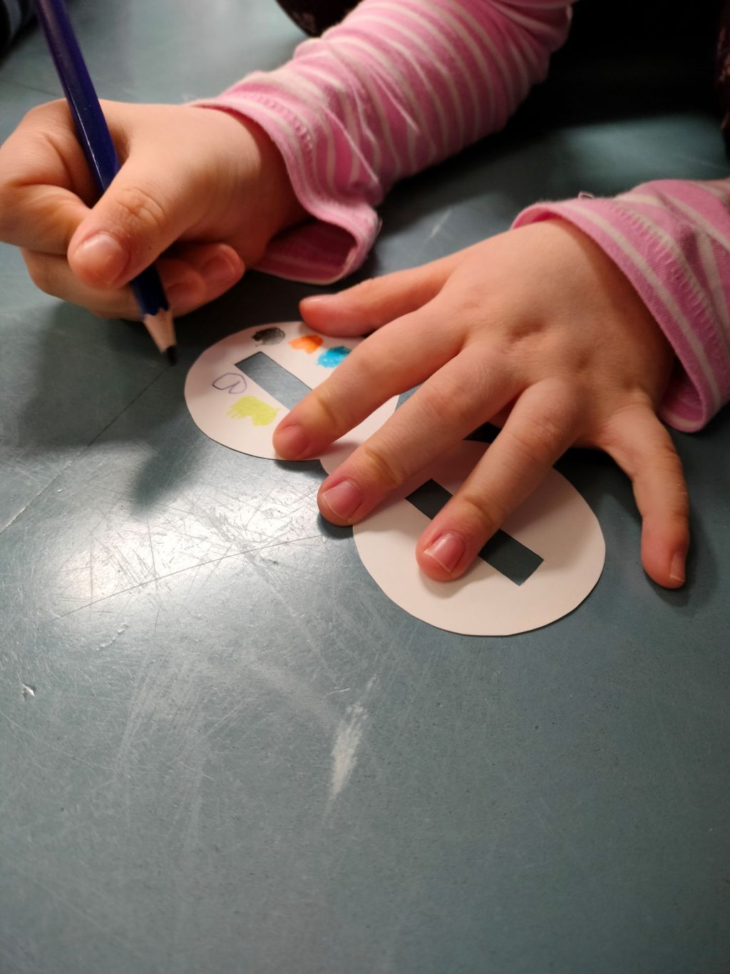 Lapsen kädet värittämässä papreista leikattua maskia.