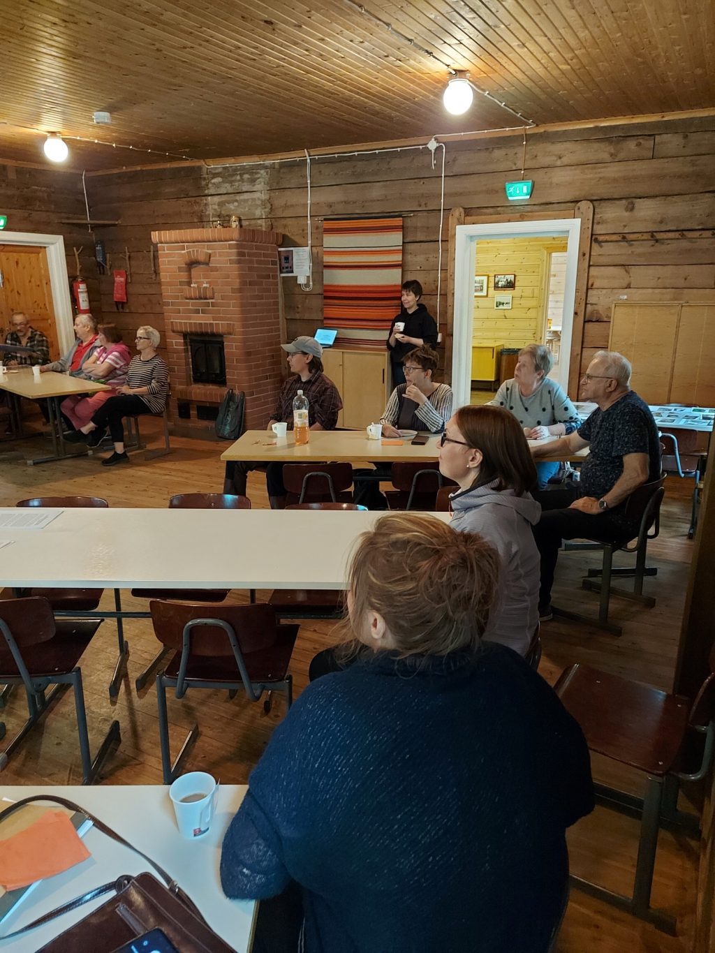 Ihmisiä istuu pöytien ääressä tumman hirsirakennuksen sisällä.