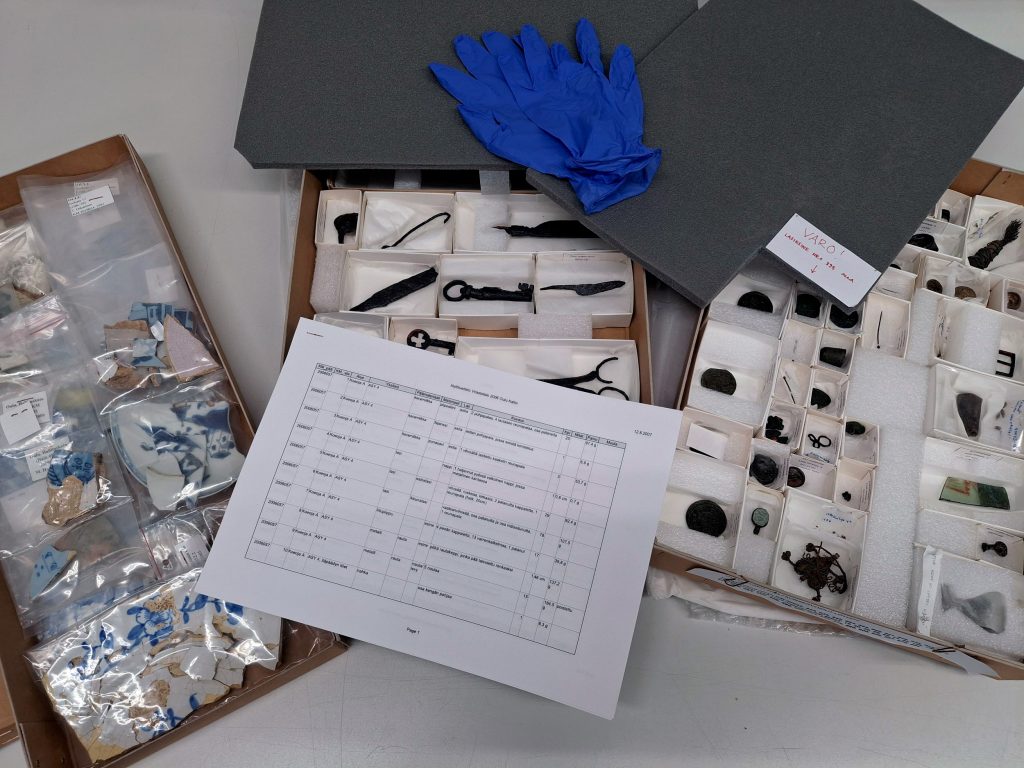 Pieniä tavaroita laatikoissa ja pusseissa. Päällä luettelo.