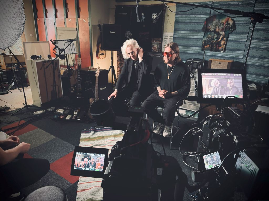 Kaksi henkilöä istuu tuoleilla ja heitä kuvataan videokameroilla.