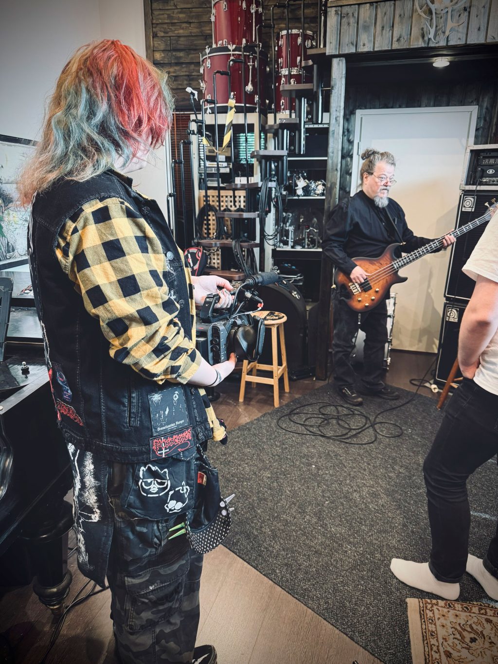 Menossa kuvaustilanne: takana henkilö kitaran kanssa ja edessä kuvaaja.