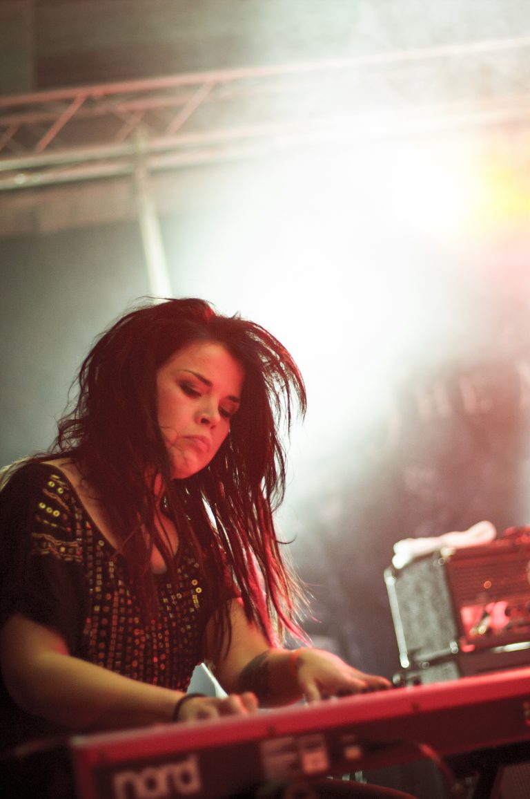 Kosketinsoittaja keskittyneenä katse koskettimilla. Taustalla kirkkaat keikkalavan valot.