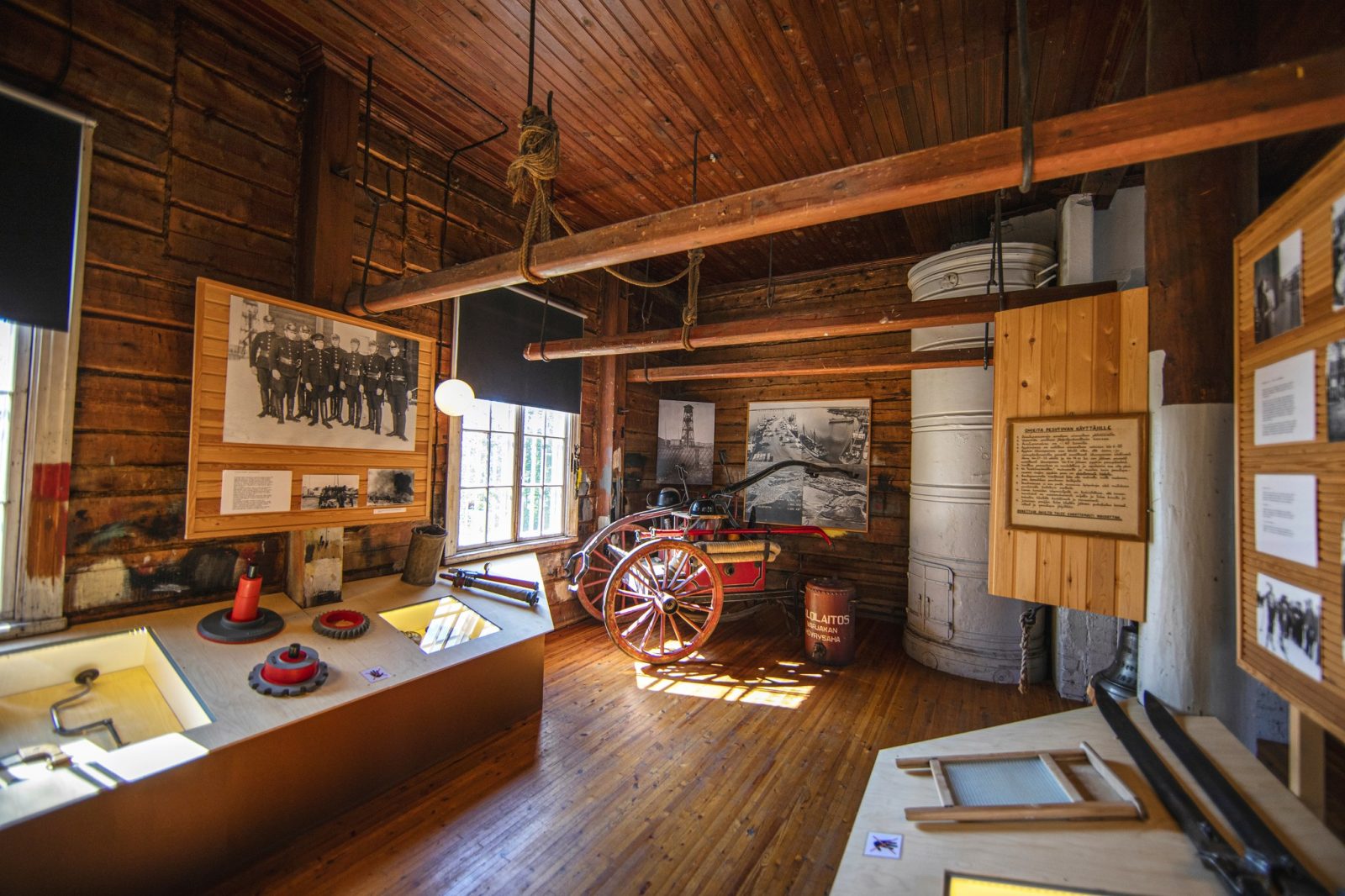 Vanhan hirsirakennuksen huoneessa museoesineitä, taustalla hevosella vedettävät palokunnan sammutuskärryt.