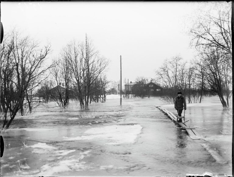 Potkukelkkailija pysähtynyt pitkospuille, joista loppuosa tulvan alla.