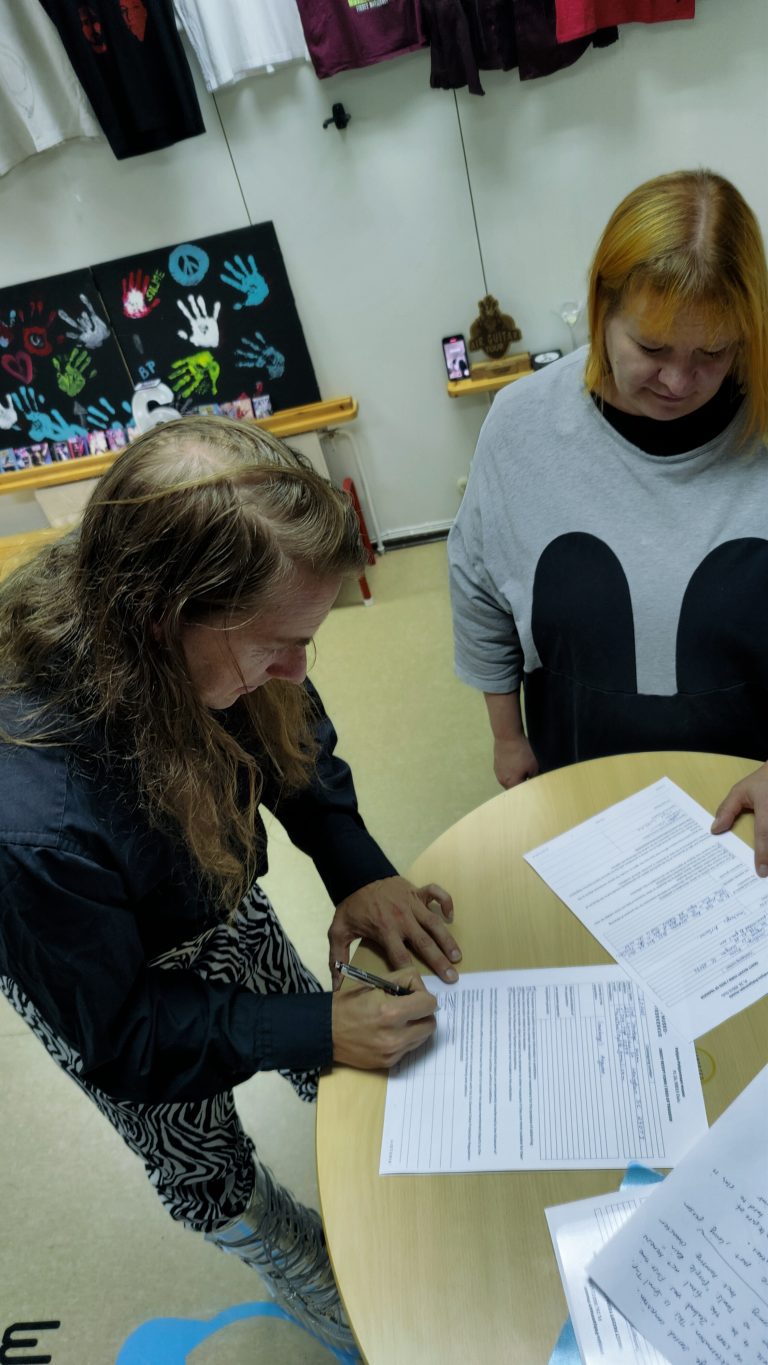 Henkilö allekirjoittaa papereita korkean pöydän ääressä.