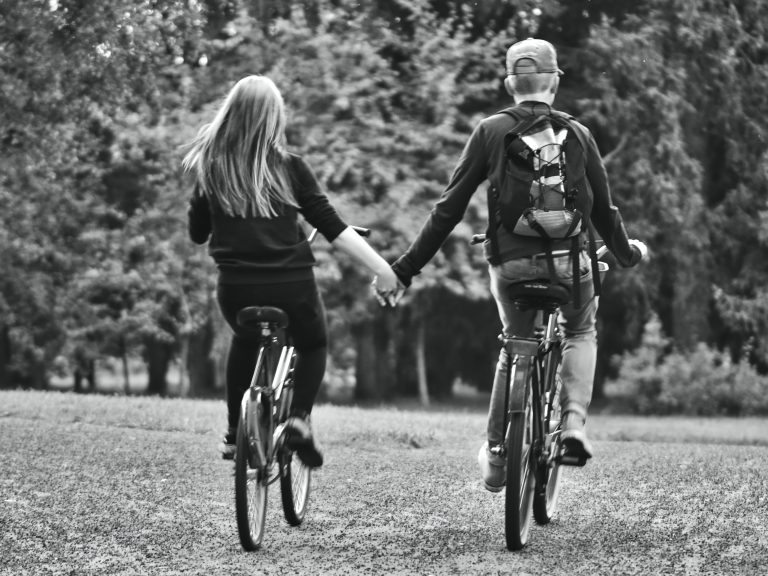 Kaksi nuorta pyöräilee käsikädessä poispäin kamerasta.