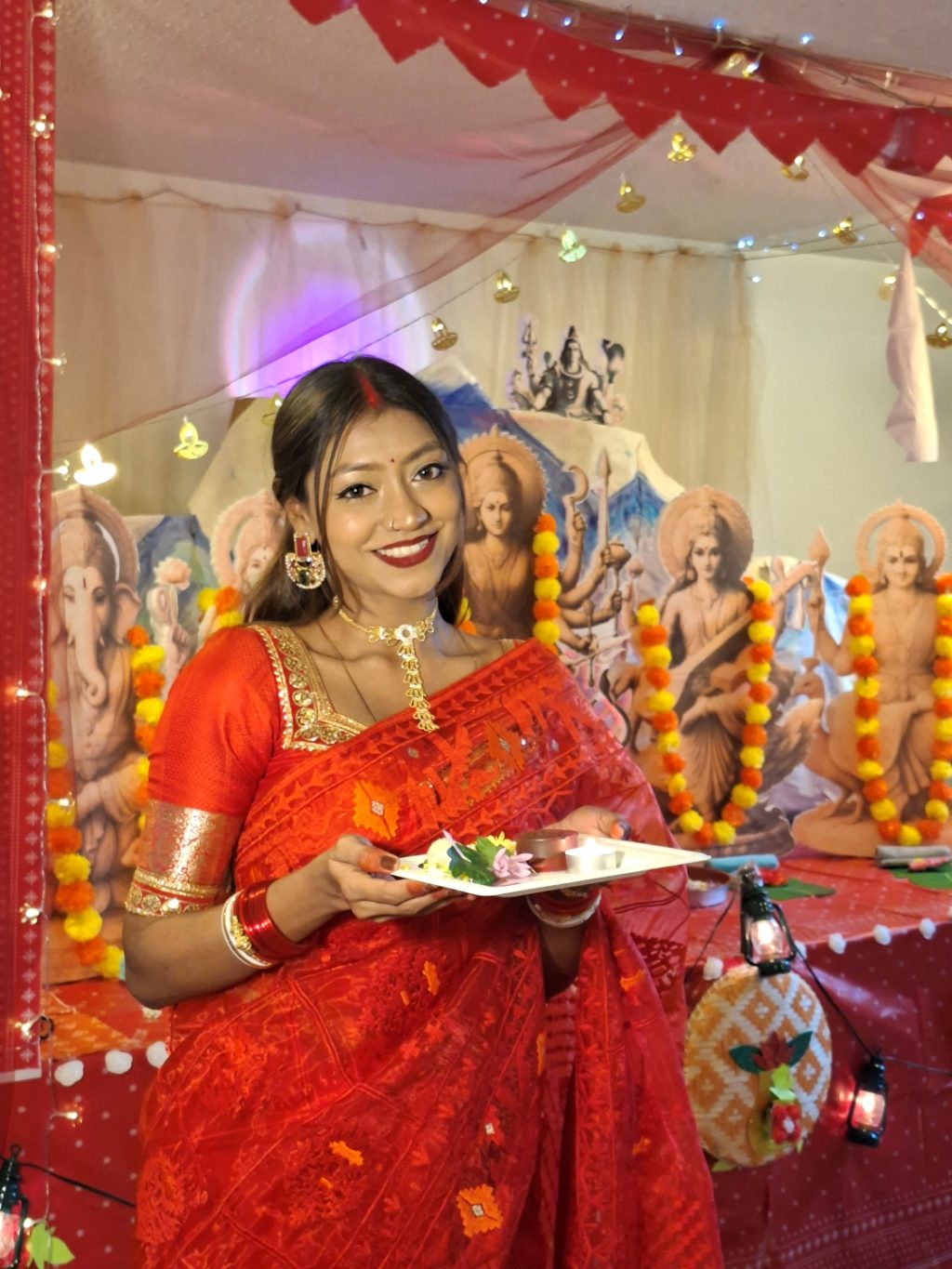 Nainen intialaisessa sarissa pitelee tarjotinta käsissään. Taustalla värikäs alttarirakennelma.