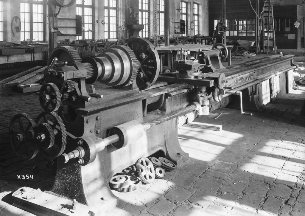 Vanhoja isoja koneita tehdashallissa, mustavalkoinen kuva.