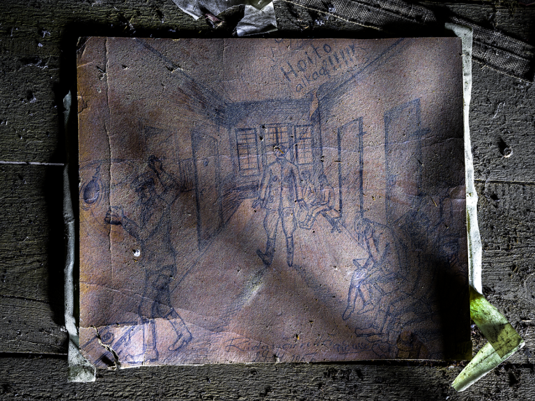 Haalistunut mustekynäpiirros vankilamaisesta sisätilasta paperilla. Perspektiivipiirros kuvaa käytävää, jonka varrella ovia ja penkeillä ihmisiä kumarassa. Kuvassa useita ihmishahmoja huoneessa,keskellä armeijamainen henkilö ja teksti "Hoito alkaa!".